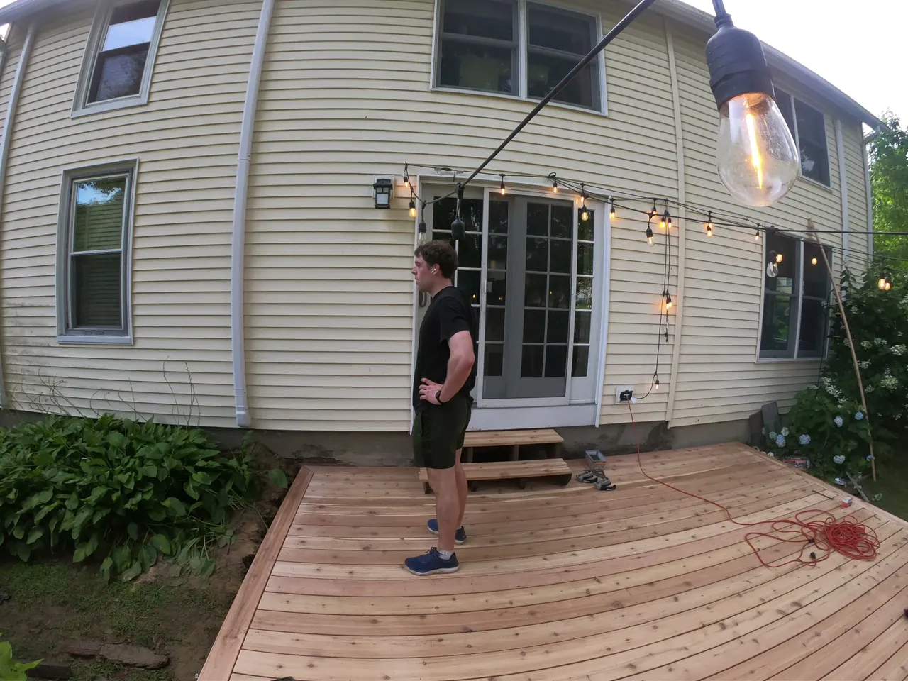 Rebuilt wood deck behind a yellow house with string lights