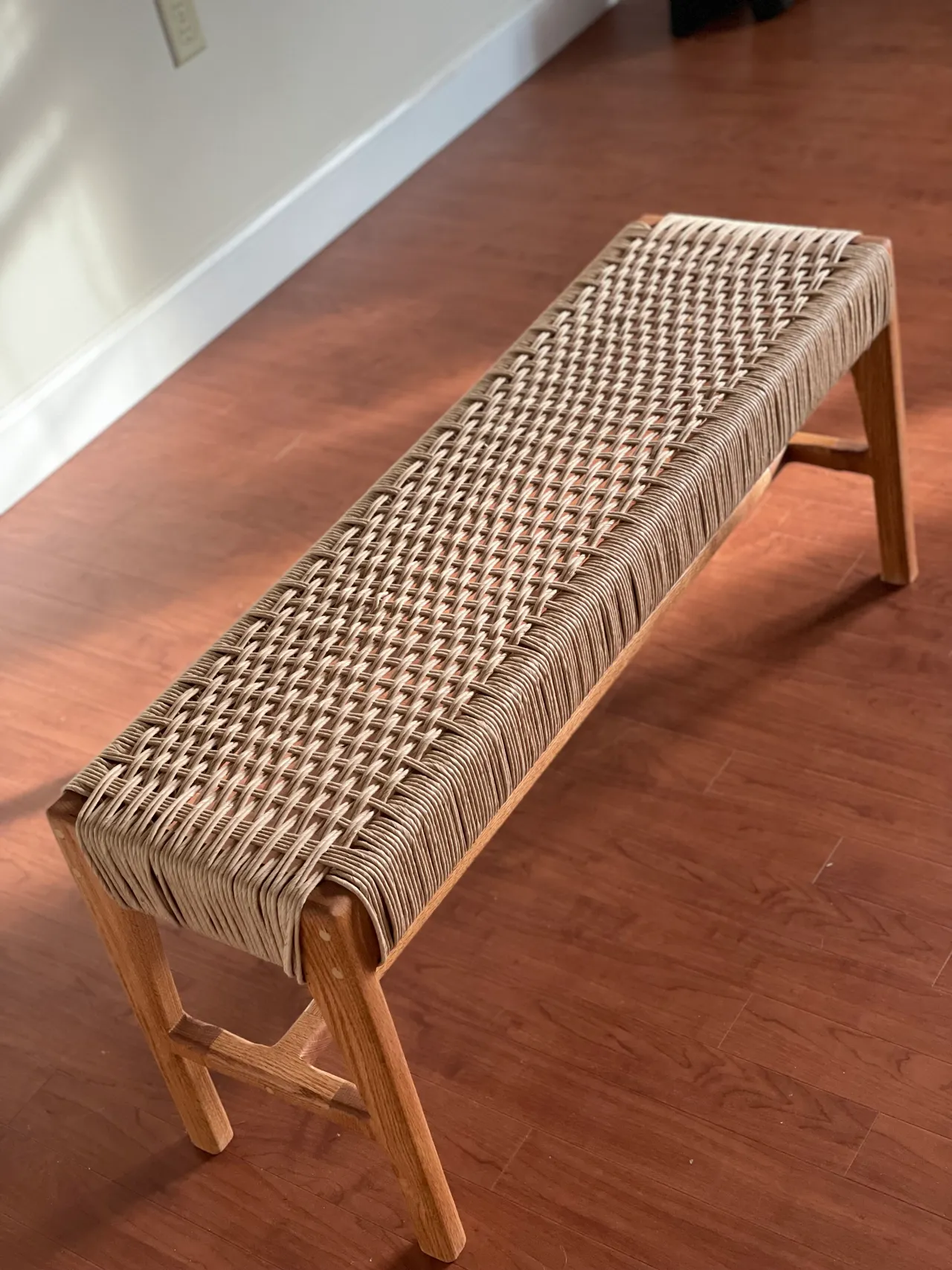 Light hardwood bench with a woven cord seat indoors