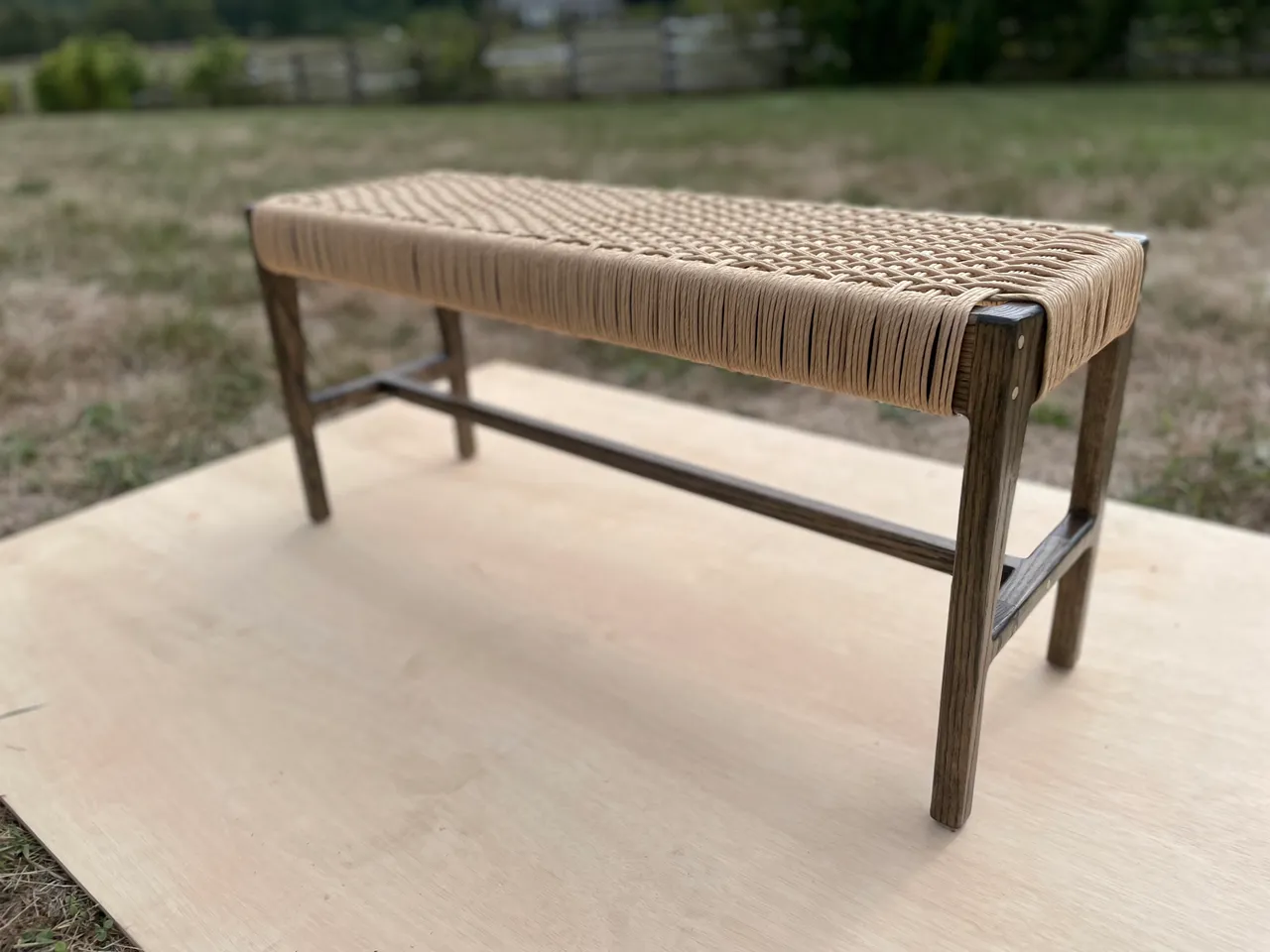 Dark-stained bench with a woven natural-cord seat, outdoors