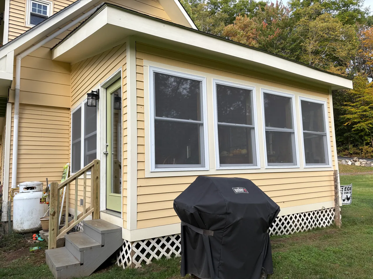 Finished yellow sunroom addition with a bank of windows and new steps